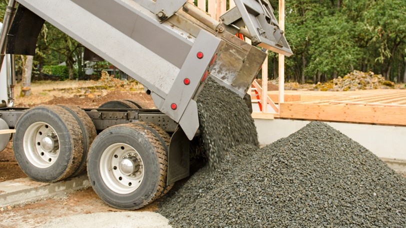 A delivery truck unloads landscaping gravel at a project site.