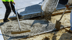 Workers use screeds and a shovel to smooth out concrete being poured.