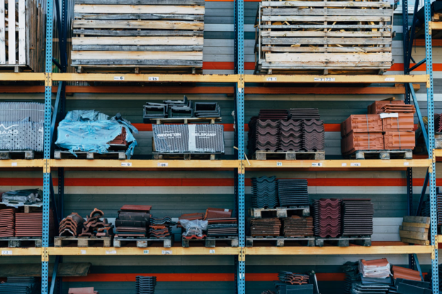 Warehouse shelving stocked with pallets of landscaping materials, including tiles, vents, and accessories, organized for construction projects.