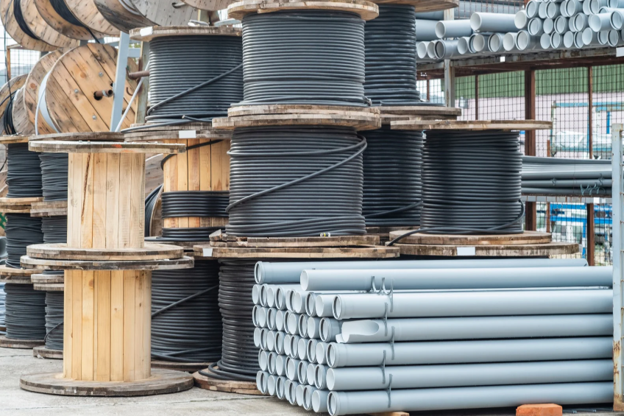 Materials supply yard with large spools of pipe, coils of tubing, and stacked PVC pipes organized for residential and commercial projects.